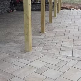 Wooden posts supporting a pergola or covered structure over a herringbone-patterned stone patio