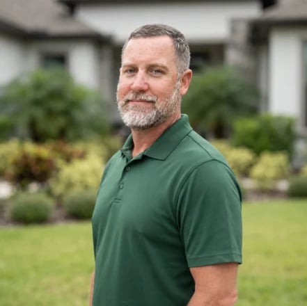 Josh Nance, owner of New Life Landscapes, wearing a green polo shirt and standing in a residential yard with lawn and landscaping